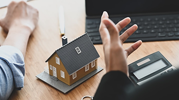 Model house and a calculator on a desk as two people discuss a home purchase
