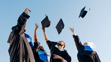 Graduates in gowns tossing their caps into a clear blue sky
