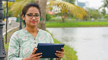 Woman holding a tablet on a riverside path in a city park
